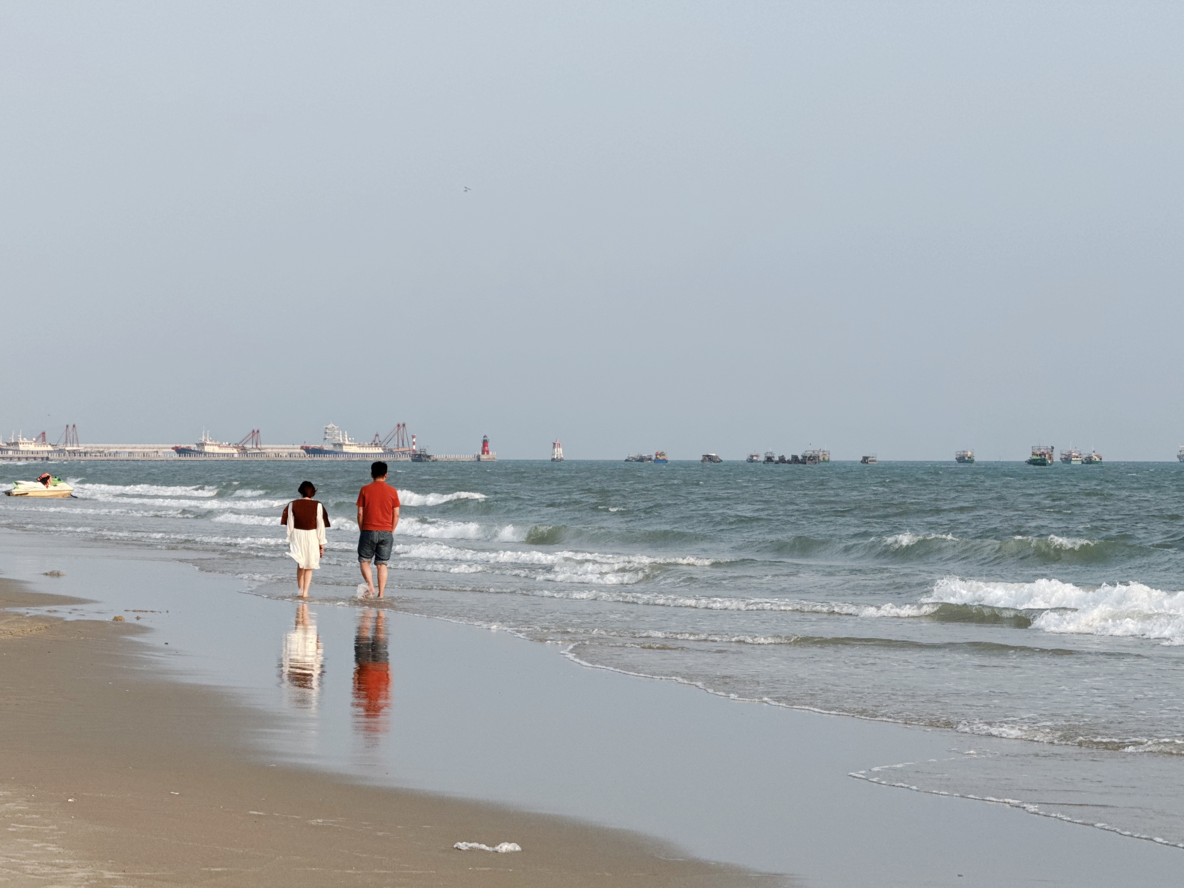 在海滩上散步的人，远处是各种大小渔船