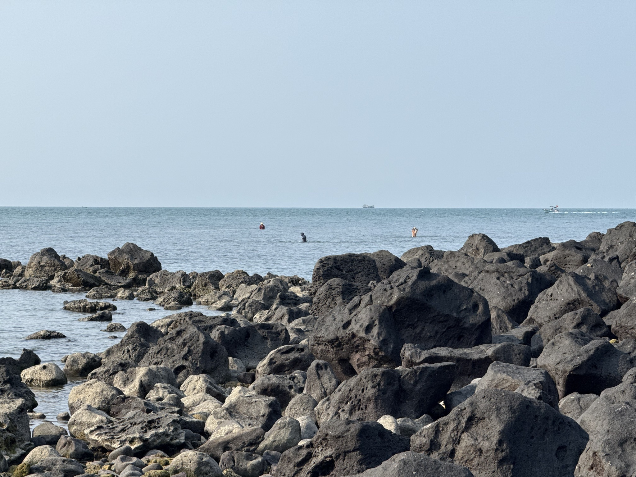 远处的海里有人在网鱼。其他人则拿着木棍在水里敲来敲去的赶鱼